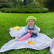 Isko joined the competition — help win amazing prizes! baby, child, green_hat, blanket, grass, outdoor, park, bottle, toy, smile, happy, nature, person, blue_overalls, striped_shirt, playtime, cute, daylight, sitting, relaxation