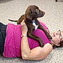 Gibson is registered to the contest to win money with this photo: black_pants, bonding, brown_dog, carpet, casual, comfort, dog, friendly, glasses, happy, home, indoor, lying_down, pet, pet_owner, puppy, purple_shirt, relaxation, watch, woman