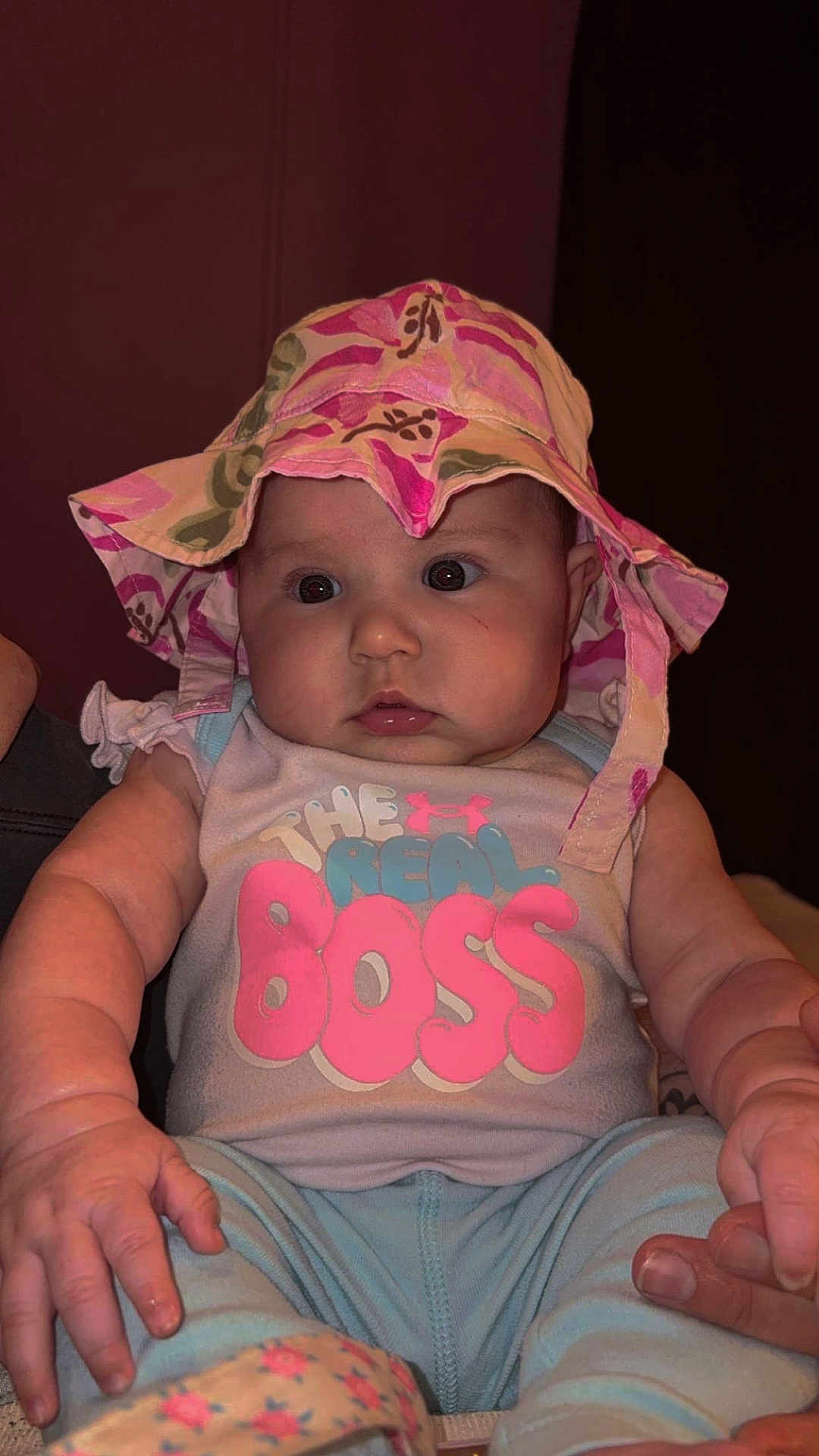 Rynlee is registered to the contest to win money with this photo: baby, infant, child, hat, bucket_hat, onesie, text_on_clothing, chubby_cheeks, big_eyes, hands, sitting, portrait, indoor, pink, blue_clothing, adorable, cute, person, closeup, soft_lighting