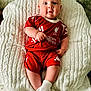 baby, blue_eyes, child, chubby_cheeks, comfortable, couch, cozy, cute, football_kit, indoor, infant, knitted_blanket, liverpool_fc, person, portrait, red_clothing, seated, smiling, soft_texture, white_socks