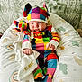 baby, baby_garment, blanket, child, colorful, colorful_clothing, cozy, cushion, cute, elmer, hat, indoor, infant, patterned_background, playful, plush_toy, portrait, seated, smiling_face, soft_toy