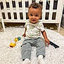 Noah participe au concours pour gagner de l'argent avec cette photo : toddler, child, curly_hair, white_rug, toy, remote_control, crib, stuffed_animals, indoor, floor, socks, pants, shirt, smiling, person, baby, cushion, home, playtime, cute