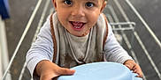 Noah participe au concours pour gagner de l'argent avec cette photo : toddler, child, shopping_cart, blue_plate, curly_hair, smiling, happy, outdoor, person, baby_bib, long_sleeve_shirt, hands, face, eyes, mouth, teeth, toy, metal_cart, urban, daylight