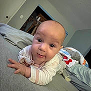 Emma is registered to the contest to win money with this photo: baby, infant, bed, blanket, clothing, face, hand, indoor, person, portrait, sleepwear, smile, toddler, young_child, room, wall, door, curiosity, expression, comfort