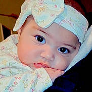 Ruth is registered to the contest to win money with this photo: baby, infant, face, headband, bow, clothing, floral_pattern, cute, closeup, resting, hand, soft_surface, portrait, child, young, indoor, person, skin, eyes, expression