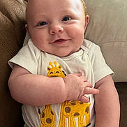 Bradlee is registered to the contest to win money with this photo: baby, infant, smile, face, blue_eyes, onesie, giraffe_print, couch, cushion, arm, hand, skin, cute, happy, child, indoor, closeup, portrait, person, comfort