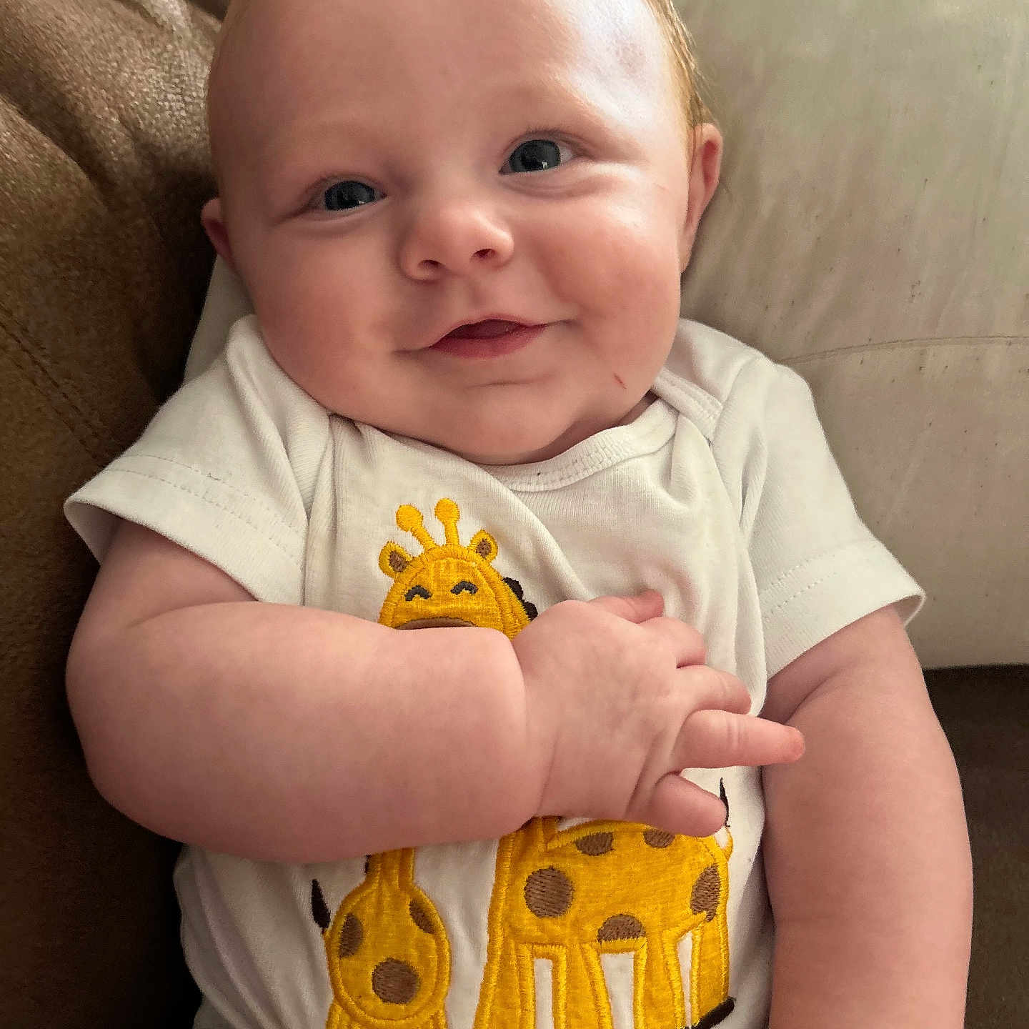 Bradlee is registered to the contest to win money with this photo: arm, baby, blue_eyes, child, closeup, comfort, couch, cushion, cute, face, giraffe_print, hand, happy, indoor, infant, onesie, person, portrait, skin, smile