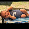 baby, infant, smiling, onesie, striped_clothing, lying_down, outdoor, inflatable, pool_float, baby_clothing, cute, child, happy, skin, face, hand, summer, sunlight, playful, portrait