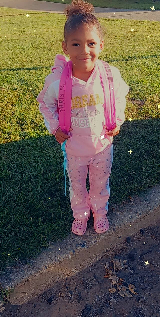 Paris is registered to the contest to win money with this photo: asphalt, baby_toddler_clothing, child, face, fun, gesture, grass, happy, head, joy, leg, leisure, magenta, people_in_nature, person, personal_protective_equipment, pink, road_surface, sleeve, smile