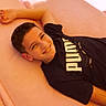 boy, casual, child, clothing, comfortable, face, happy, indoors, leisure, lying_down, person, pink_background, portrait, puma, relaxed, resting, short_hair, smiling, tshirt, young