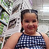 Monserrat joined the competition — help win amazing prizes! child, girl, smiling, braided_hair, earrings, blue_dress, checkered_pattern, store, aisle, boxes, home_goods, garden, snack, casual, portrait, shopping, indoor, young, happy, cute