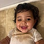 baby, infant, child, smiling, curly_hair, drooling, stained_shirt, onesie, closeup, portrait, happy, chubby_cheeks, eyes, mouth_open, tongue, lying_down, floor, tiles, indoor, cute