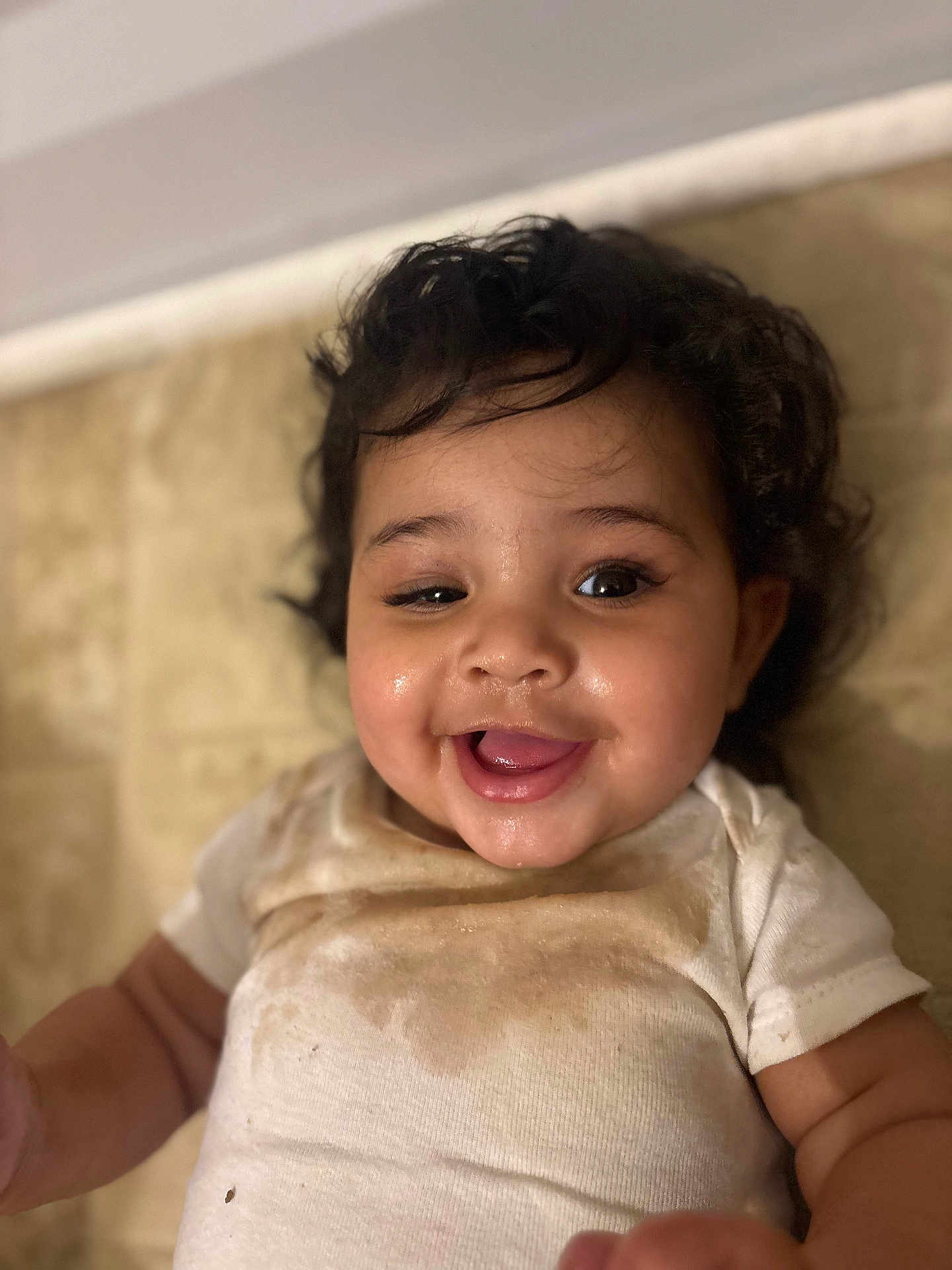 Leilani joined the competition — help win amazing prizes! baby, infant, child, smiling, curly_hair, drooling, stained_shirt, onesie, closeup, portrait, happy, chubby_cheeks, eyes, mouth_open, tongue, lying_down, floor, tiles, indoor, cute