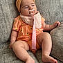 baby, sleeping, pacifier, headband, orange_clothing, pineapple_pattern, bib, couch, soft_furniture, infant, chubby_legs, relaxed, indoors, comfort, cute, peaceful, child, toddler, resting, adorable