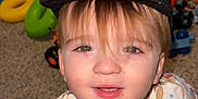 Kaizer is registered to the contest to win money with this photo: toddler, child, cap, pajamas, smiling, face, toy_car, playroom, carpet, hot_dog_pattern, baseball_pattern, indoor, cute, young_child, hair, eyes, toy, colorful, floor, happy