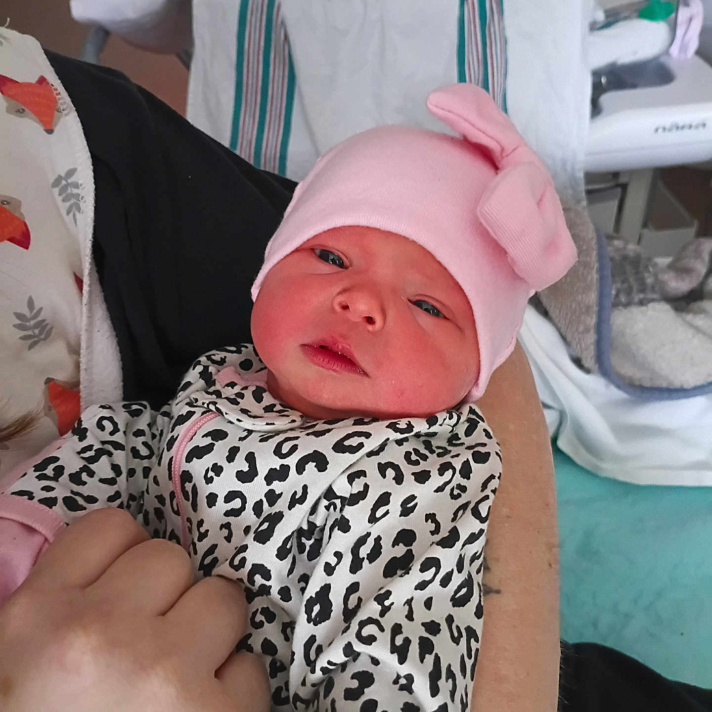 Rebecca is registered to the contest to win money with this photo: newborn, baby, infant, pink_hat, bow, leopard_print, onesie, hand, hospital, bed, blanket, person, skin, clothing, baby_gear, indoor, cute, face, holding, newborn_baby