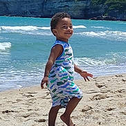 İbrahim joined the competition — help win amazing prizes! child, toddler, smiling, beach, sand, ocean, waves, cliff, greenery, blue_sky, sunlight, summer, vacation, barefoot, romper, portrait, playing, seashore, footprints, outdoor