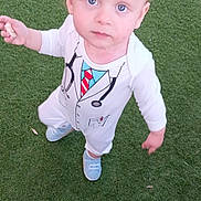 Aylan participe au concours pour gagner de l'argent avec cette photo : toddler, child, grass, outdoor, blue_eyes, white_clothing, doctor_costume, snack, standing, curious, baby_shoes, young_child, playful, portrait, casual, daylight, person, looking_up, cute, innocent