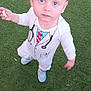 toddler, child, grass, outdoor, blue_eyes, white_clothing, doctor_costume, snack, standing, curious, baby_shoes, young_child, playful, portrait, casual, daylight, person, looking_up, cute, innocent