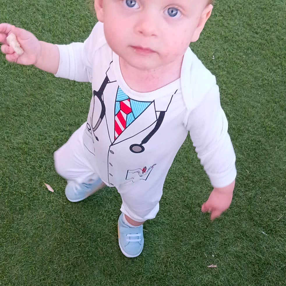 Aylan participe au concours pour gagner de l'argent avec cette photo : baby_shoes, blue_eyes, casual, child, curious, cute, daylight, doctor_costume, grass, innocent, looking_up, outdoor, person, playful, portrait, snack, standing, toddler, white_clothing, young_child