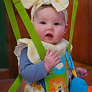 Lucia joined the competition — help win amazing prizes! baby, child, headband, bow, harness, colorful_clothing, lion_patch, indoor, curious, face, hands, soft_light, playful, cute, infant, person, seated, toy, fabric, portrait
