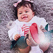 Jazara is registered to the contest to win money with this photo: baby, smiling, pink_bow, hair_accessory, white_outfit, red_design, colorful_shoes, fluffy_cushion, gray_cushion, child, indoor, portrait, happy, cute, infant, sitting, soft_texture, cozy, person, young_child