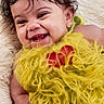 baby, smiling, curly_hair, green_bows, yellow_outfit, red_heart, fluffy_clothing, lying_down, soft_blanket, infant, cute, happy, portrait, child, adorable, face, skin, earrings, closeup, warm_lighting