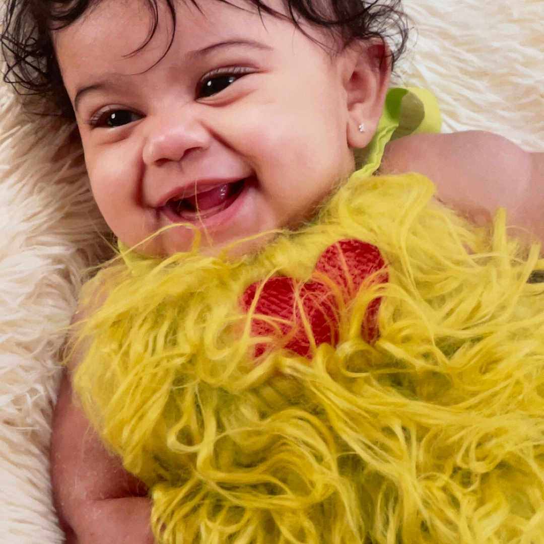 Jazara joined the competition — help win amazing prizes! baby, smiling, curly_hair, green_bows, yellow_outfit, red_heart, fluffy_clothing, lying_down, soft_blanket, infant, cute, happy, portrait, child, adorable, face, skin, earrings, closeup, warm_lighting