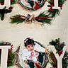 baby, child, basket, christmas, holiday, joy, decorations, pine_cones, red_berries, greenery, white_outfit, pink_bow, socks, shoes, fuzzy_background, portrait, festive, cute, indoor, smiling