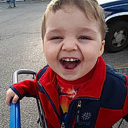 Robbie joined the competition — help win amazing prizes! child, toddler, smiling, shopping_cart, red_jacket, outdoor, parking_lot, vehicle, grocery_store, happy, face, person, casual_clothing, daylight, retail, playful, young_child, expression, holding, fun
