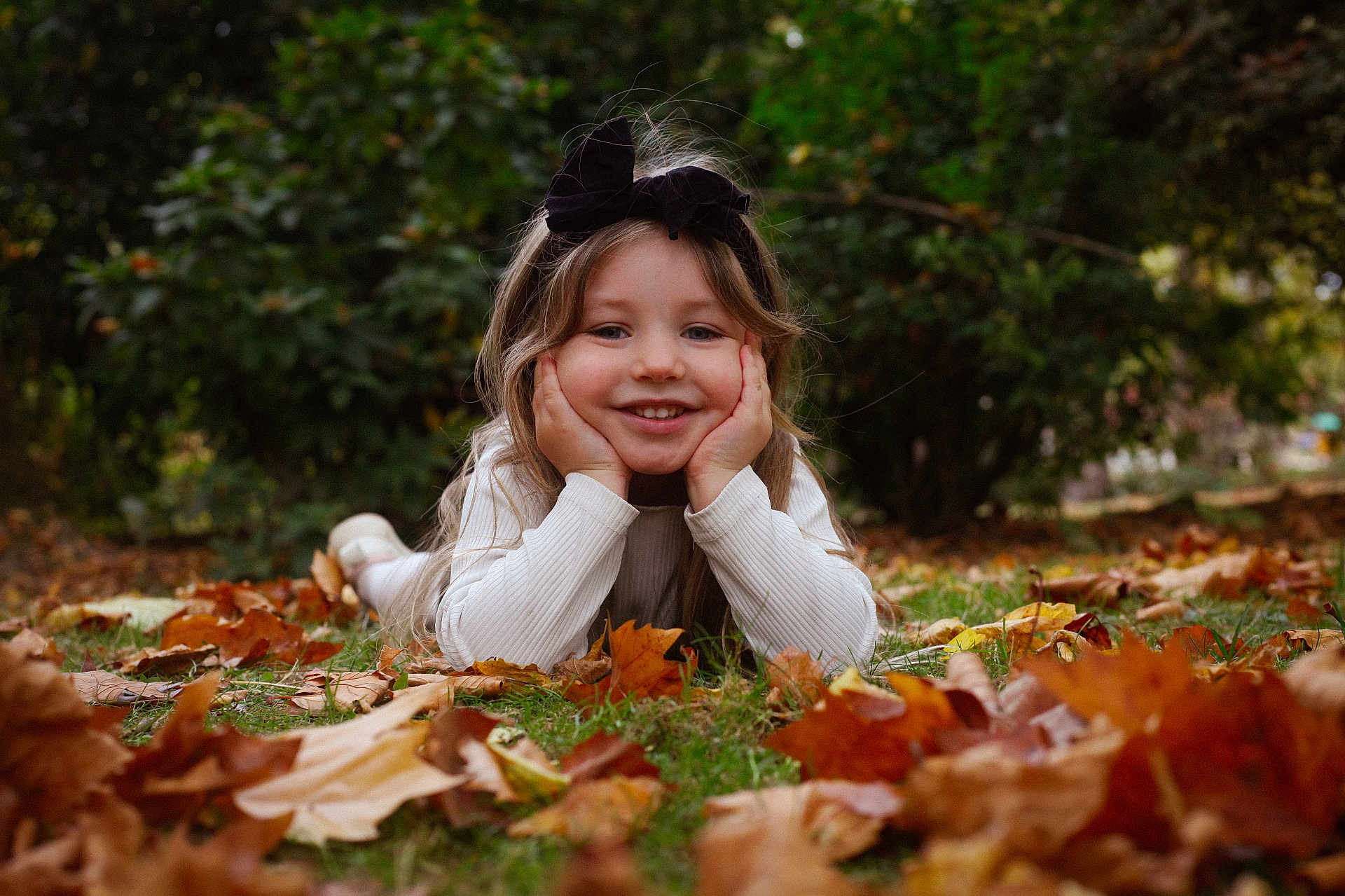 Mélina a rejoint le concours — aidez-le/la à gagner de superbes lots ! autumn, child, face, fall, girl, grass, greenery, hair_bow, hands, happy, leaves, lying_down, nature, outdoor, playful, portrait, seasonal, smile, white_sweater, young