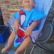 Loukas participe au concours pour gagner de l'argent avec cette photo : baby, barefoot, black_dog, brick_wall, child, clothing, concrete_floor, dog, happy, high_chair, laughing, metal_frame, outdoor, person, playful, seat, smiling, spiderman, toddler, towel
