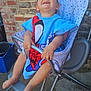 baby, barefoot, black_dog, brick_wall, child, clothing, concrete_floor, dog, happy, high_chair, laughing, metal_frame, outdoor, person, playful, seat, smiling, spiderman, toddler, towel