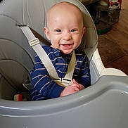 Connor is registered to the contest to win money with this photo: baby, high_chair, smile, child, indoor, seat, clothing, striped, face, happy, infant, person, home, wood_floor, heater, can, table, hands, cute, seatbelt