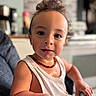 Julian is registered to the contest to win money with this photo: toddler, child, face, eyes, hair, necklace, tank_top, high_chair, indoor, kitchen, person, portrait, skin, expression, curious, sitting, hand, furniture, background, home