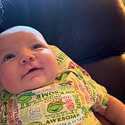 Tatum joined the competition — help win amazing prizes! baby, infant, child, face, smile, clothing, onesie, colorful, text, pattern, couch, leather, indoor, portrait, cute, happy, looking_up, soft_light, chubby_cheeks, resting
