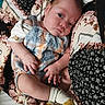 baby, infant, child, plaid, romper, socks, blanket, floral_pattern, face, skin, hand, foot, lying_down, curious, indoors, closeup, cute, soft_texture, cozy, portrait