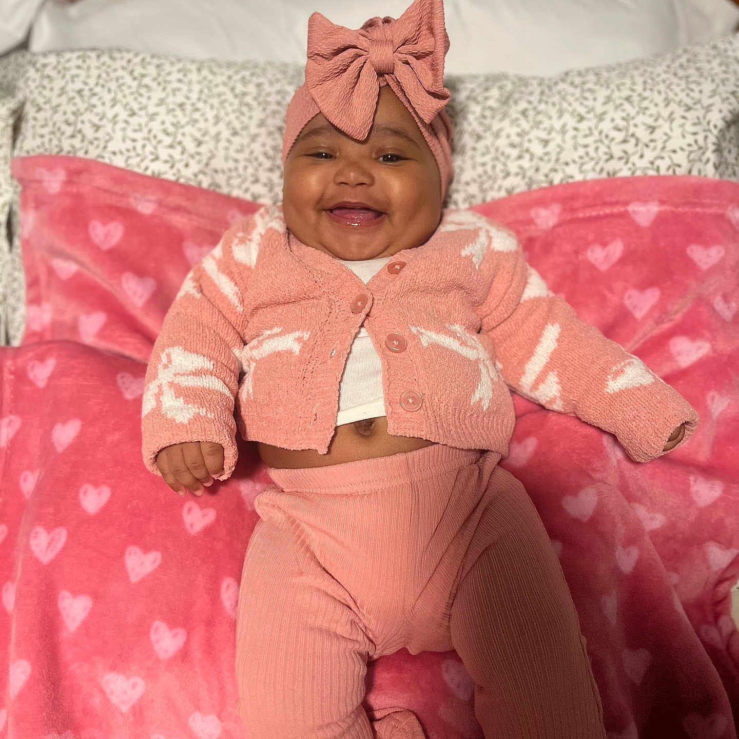 Brailee Beachum joined the competition — help win amazing prizes! baby, bed, bow, cardigan, clothing, cozy, cute, hand, happy, headband, heart_pattern, infant, lying_down, nursery, pants, pillow, pink_blanket, portrait, smile, soft_toy_style