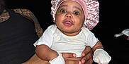 Brailee Beachum is registered to the contest to win money with this photo: baby, infant, bonnet, mittens, diaper, white_onesie, adult_hand, couch, black_sofa, red_shorts, socks, wide_eyes, smile, portrait, sitting, indoor, window_blinds, door, tattoo, flash_photography