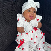Brailee Beachum is registered to the contest to win money with this photo: baby, infant, girl, headwrap, bow, mittens, heart_pattern, white_dress, blanket, footprints, couch, smile, portrait, closeup, sitting, adorable, cute, dark_background, red_bow, leggings