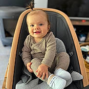April participe au concours pour gagner de l'argent avec cette photo : baby, child, smiling, indoor, baby_chair, clothing, footwear, person, cute, happy, portrait, infant, small_hands, light_brown_hair, baby_girl, cozy, soft_lighting, wooden_frame, cushion, casual_wear