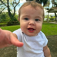 Levi is registered to the contest to win money with this photo: toddler, child, baby, smiling, white_shirt, outdoor, grass, trees, nature, portrait, cute, happy, face, person, short_hair, daylight, greenery, playful, reaching_hand, casual_clothing