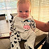 baby, infant, cow_print, onesie, table, wood, curtains, window, sunlight, person, arm, milk_bottle, phone, indoor, child, cute, expression, sitting, clothing, home