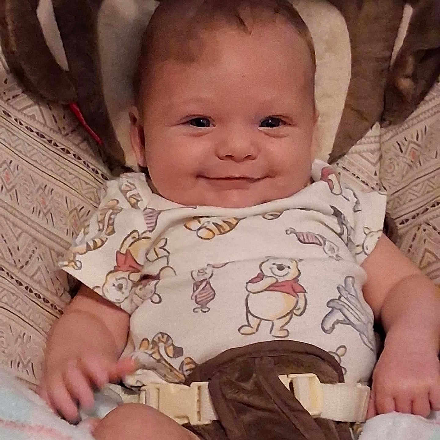 Levi joined the competition — help win amazing prizes! baby, smiling, infant, onesie, winnie_the_pooh, baby_carrier, blanket, cushion, clothing, cute, happy, child, person, portrait, indoors, seat_belt, baby_boy, young_child, comfort, face
