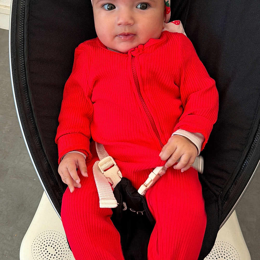 Belsame participe au concours pour gagner de l'argent avec cette photo : baby, baby_rocker, buckle, carpet, child, clothing, curious, cute, floor, footwear, hands, headband, indoor, infant, person, portrait, red_onesie, seated, slippers, strawberry_pattern
