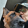 Panda participe au concours pour gagner de l'argent avec cette photo : dog, german_shepherd, person, glasses, cap, close_up, face, affection, outdoor, pet, animal, portrait, brown_fur, black_fur, hand, love, companionship, snout, eyes, candid