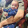Oakley joined the competition — help win amazing prizes! baby, man, beard, smile, blue_clothing, onesie, chair, arm, indoor, person, seated, red_chair, facial_expression, baby_clothes, holding, casual_wear, furniture, happy, human, parent