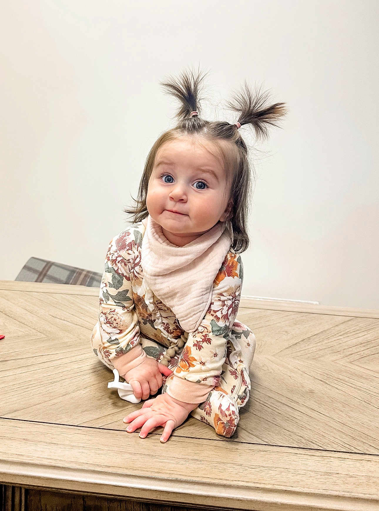 Monroe is registered to the contest to win money with this photo: child, baby, toddler, pigtails, floral_onesie, bib, pacifier, wooden_table, hands, big_eyes, chubby_cheeks, indoor, neutral_background, portrait, sitting, cute, playful, hair_ties, soft_lighting, clothing