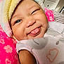 Layla is registered to the contest to win money with this photo: baby, infant, face, tongue, wink, blanket, towel, pink, soft, cozy, cute, smile, child, indoors, sleepwear, fuzzy, person, headwear, expression, closeup