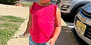 Layla is registered to the contest to win money with this photo: toddler, child, yellow_hat, red_shirt, blue_shorts, white_shoes, outdoor, sidewalk, sunny, daytime, parked_cars, greenery, smiling, walking, person, casual_clothing, hat, cheerful, holding_object, urban